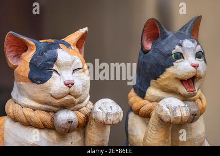 tokio, japan - februar 28 2021: Nahaufnahme von aum Paar von zwei hölzernen geschlossenen und offenen Maul-Statuen, die japanische Maneki-Neko-Katzen mit einem Stockfoto