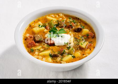 Rassolnik, Rind-, Gerste-, Karotten- und Gurkensuppe. Gekocht in salzig-saurer Gurkenbasis. Serviert in weißer Schale auf elfenbeinfarbener Stofftischdecke. Mit Stil Stockfoto