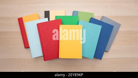 Draufsicht auf einen Stapel von bunten Büchern, die auf einem hellen Holzschreibtisch zentriert sind. Stockfoto
