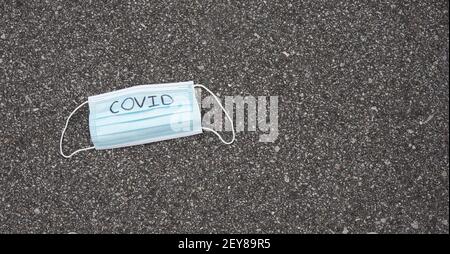 Maske mit dem darauf aufgeschriebenen Wort covid, das auf Asphalt mit dem Kopierraum liegt. Stockfoto