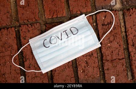 Maske mit dem auf sie aufgeschriebenen Wort covid, das auf den Ziegelschritt gelegt ist. Stockfoto
