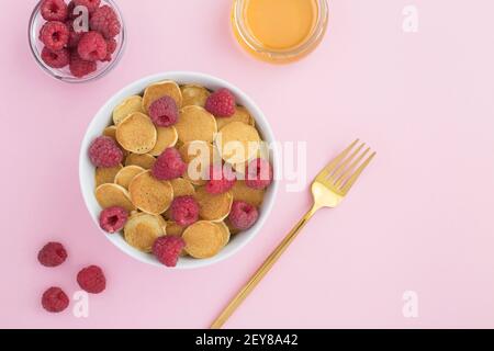 Draufsicht auf Mini-Pfannkuchen mit Himbeeren in weiß Schüssel auf der rosa Oberfläche Stockfoto