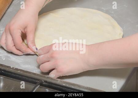 Hände des Kochs legen gerollten Teig auf Form für die Herstellung von Knödeln. Kochvorgang von hausgemachten Ravioli. Stockfoto