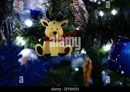 Niedliche Weihnachtsdekoration in Form eines kleinen weißen Rentiers mit einem Schal, der an einem Weihnachtsbaum hängt Stockfoto