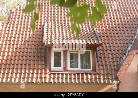 Fenster im alten Dachboden mit Ziegeldach. Teil eines Fassadengebäudes aus dem letzten Jahrhundert. Selektiver Fokus. Stockfoto