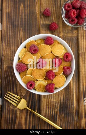 Draufsicht auf Mini-Pfannkuchen mit Himbeeren in der weißen Schüssel auf dem Holztisch. Position vertikal. Stockfoto