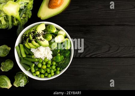 Vegane Poke Schüssel mit weißem Reis und grünem Gemüse in der weißen Schüssel auf dem schwarzen Holzhintergrund.Draufsicht. Speicherplatz kopieren. Stockfoto