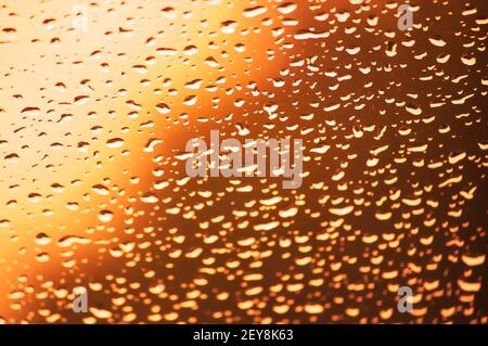 Entkochte Tropfen der Flüssigkeit auf das Fensterglas mit goldenes Licht im Hintergrund Stockfoto