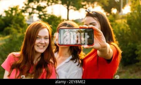 Drei junge Freundinnen fotografieren sich am sonnigen Sommertag am Handy. Außenportrait von drei Freunden, die Fotos mit machen Stockfoto