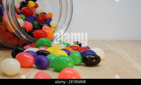 Bunte Jelly Beans, die aus einem Glas auf den Tisch auslaufen. Leerzeichen in der oberen Ecke für die Nachricht Stockfoto