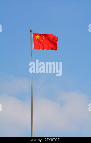 Leuchtend rote chinesische Nationalflagge weht im Wind gegen einen blauen Himmel. Stockfoto