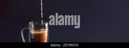 Banner mit Milch Gießen in schwarzen Kaffee in Glas Tasse auf dunkelblauem Hintergrund. Nahaufnahme Kaffee Liebe Konzept. Vorderansicht Stockfoto