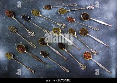 Ein Blick von oben auf Vintage Besteck Löffel mit verschiedenen Arten Von trockenen Teeblättern auf blauem Hintergrund Stockfoto