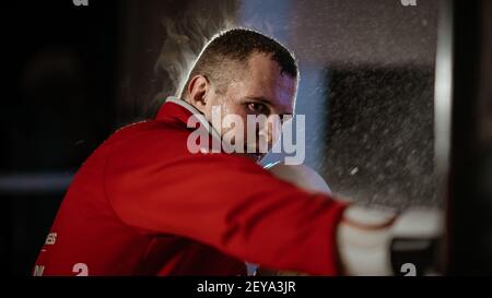 Ein schwitzender männlicher Kampfkünstler trifft mit auf den Boxsack Handschuhe Stockfoto