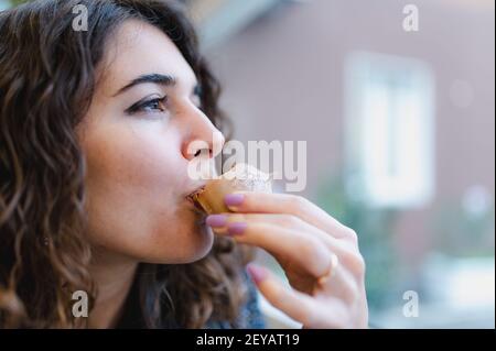 Ein flacher Fokus einer lockigen jungen Brünette weiblich essen Ein Schokoladenbonbon Stockfoto