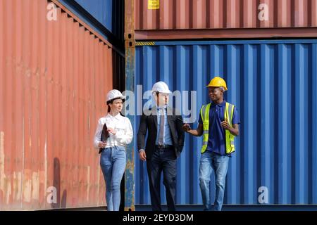 afroamerikanischer Vorarbeiter erklärt einem kaukasischen Manager die verschiedenen Abschnitte des Containerdepot-Terminals mit einer Sekretärin daneben Stockfoto