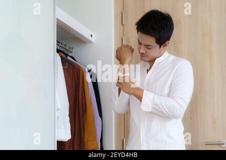 Asiatische Mann sind knöpfte ihre Hemden, um sich anzuziehen, immer bereit, um am Morgen in der Garderobe zu Hause zur Arbeit zu gehen. Stockfoto