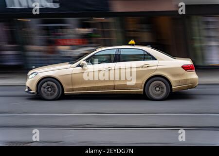 Würzburg, DEUTSCHLAND - 22. Jan 2021: Ein gelbes Taxi fährt schnell durch die Straße. Ein mercedes fährt auf Bahngleisen Stockfoto