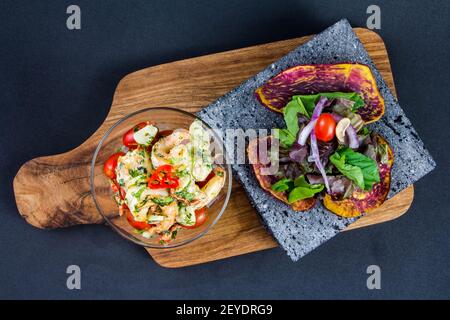 Lecker gebratene Garnelen in einer gusseisernen Pfanne mit Petersilie und Knoblauch, Chili, Tomate mit Zitrone auf schwarzem Hintergrund Stockfoto