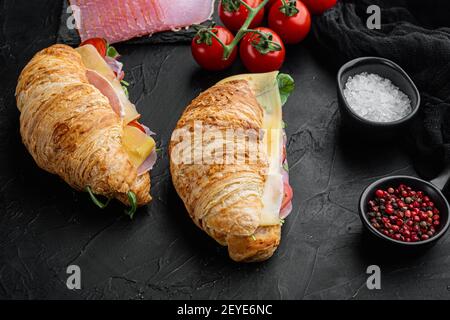 Croissant-Sandwich mit Prosciutto, Tomaten, Käse-Set, mit Kräutern und Zutaten, auf schwarzem Stein Hintergrund Stockfoto