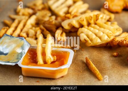 Schnelles, praktisches Fastfood-Bild mit selektivem Nahaufnahme-Fokus Von Rüschen Waffel Kartoffelfries in eine kleine Packung getaucht Von Soße mit anderen liegend Stockfoto