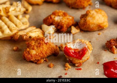 Schnelles, praktisches Fast-Food-Bild mit Nahaufnahme, selektiver Fokus auf gebissene, frittierte Hähnchennuggets, die in Ketchup mit roten Tomaten auf Backpapier getaucht wurden. R Stockfoto