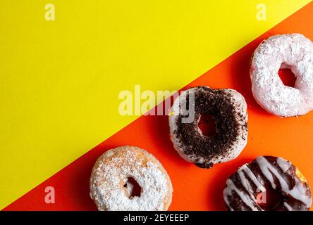 Sortiment von dekorativen süßen frisch gebackenen Donuts auf zweifarbigem Hintergrund. Die Wüsten mit verschiedenen Ausführungen und Belägen sind auf oranger Seite whi Stockfoto