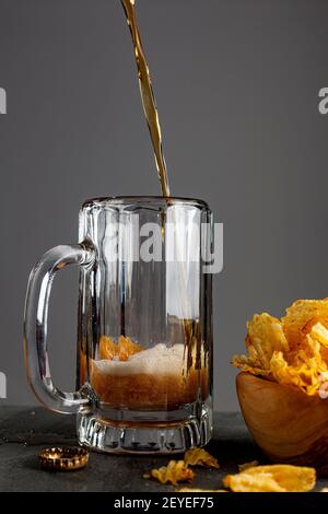 Craft Beer wird in einem Glas Becher mit Griff in einem Pub mit dunklem Hintergrund gegossen. Es schäumt und macht funkelt, wie das Glas füllt sich. Es gibt einen Arbeitsauftrag Stockfoto