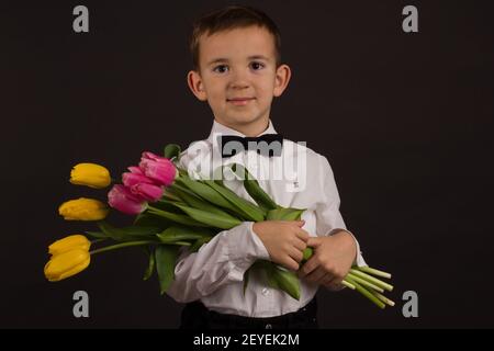 Der Junge mit Vitiligo in einem weißen Hemd und ein Fliege mit Tulpen auf schwarzem Studio-Hintergrund Stockfoto