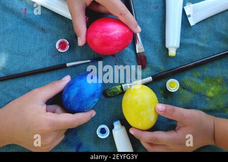 Ostersonntag Ei Malerei Aktivitätskonzept. Kinder Hände malen bunte Eier auf Tisch flach legen. Stockfoto