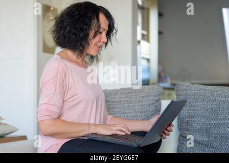 Frau arbeitet an ihrem Computer und lächelt an der Computer in einer Seitenansicht Stockfoto