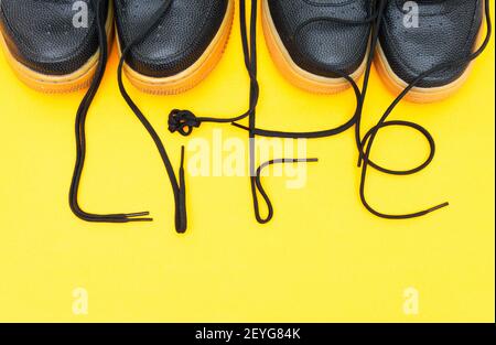 Crop-Ansicht von zwei Paaren von ähnlichen Sneakers mit dem Wort LEBEN aus den Schnürsenkeln auf einem gelben Hintergrund gemacht. Stockfoto