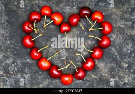 Reife rote Süßkirschen in Form eines großen Herzens auf einem grungigen Tisch angeordnet. Romantisches Liebeskonzept. Stockfoto