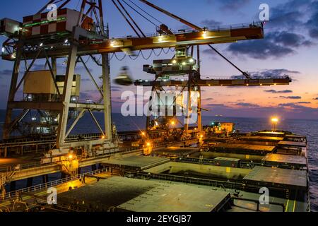 Hafenkrane entladen nachts Kohle vom Schiff. Stockfoto