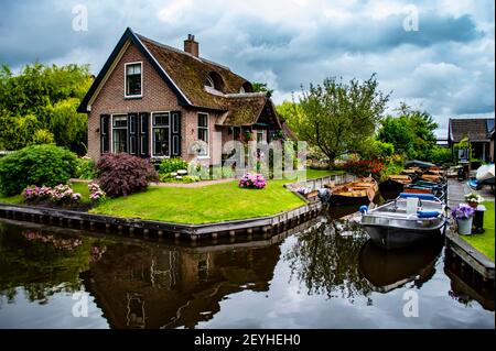 Giethoorn, Niederlande - 6. Juli 2019: Ländliches holländisches Haus mit traditionellem Dach und Motorbooten, die in den Kanälen des Dorfes Giethoorn, bekannt als die, angedockt sind Stockfoto