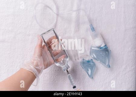 Textil weiß Hintergrund und eine Hand in einem medizinischen Handschuh zeichnet eine Kochsalzlösung für einen Vernebler mit einer Spritze. Stockfoto