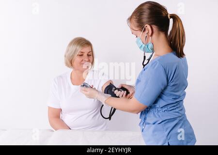 Eine Krankenschwester misst den Blutdruck mit einem medizinischen digitalen Blutdruckmessgerät. Ältere Menschen Kardiologie Gesundheitswesen Konzept auf weiß Stockfoto