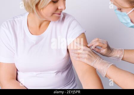 Hausarzt Impfung weibliche Patientin in der Klinik. Arzt, der der älteren Frau im Krankenhaus eine Injektion verabreichung gab. Krankenschwester hält Spritze mit Covid-19 Stockfoto