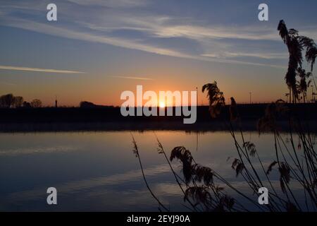 Morgensonnengang über dem Fluss in der Nähe von Oss, Niederlande mit Schilf am Flussufer im Vordergrund Stockfoto