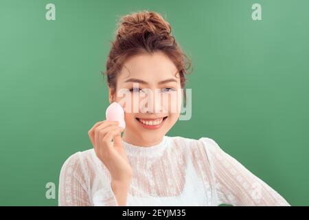 Frau, die Foundation mit kosmetischen Schwamm, Beauty-Mixer. Foto von Frau mit perfektem Make-up auf grünem Hintergrund Stockfoto