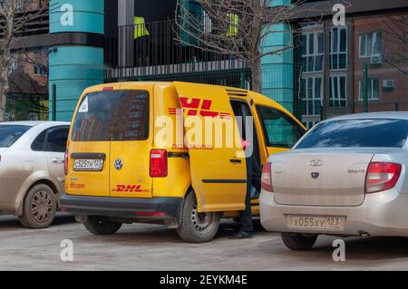 Krasnodar, Russland - März 4 2021: DHL Lieferung gelb Van ist geparkt, die Tür ist offen und der Lieferfahrer sucht das Paket. Stockfoto