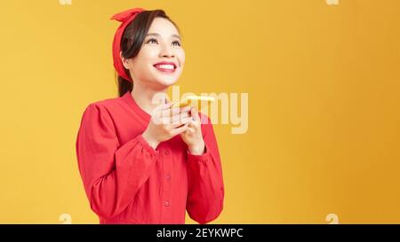 Glückliche Frau mit Spracherkennung auf Handy über gelb Hintergrund Stockfoto