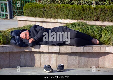 Ein Chinese, der ein Nickerchen macht, wird dies überall und jederzeit tun. Schuhe aus und auf einer öffentlichen Bank sieht aus wie Obdachlose oder arme Person. Stockfoto