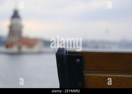 Ecke der Straßenbank aus Holz und Metall zusammen mit verschwommenem Jungfernturm istanbul Hintergrund und bosporus Meer während bewölkten Himmel Hintergrund. Stockfoto