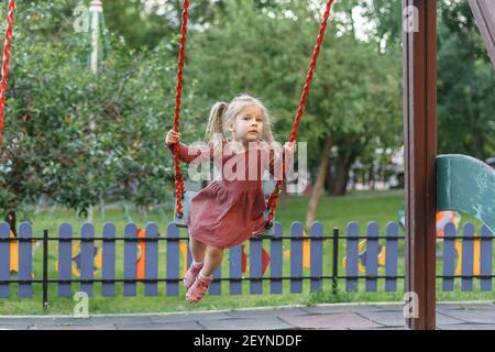 kaukasische Kind Mädchen in roten Polka dot Kleid schwingen auf einer Schaukel an einem Sommertag. Sommer Kinder Spiele und Spaß im Freien. Stockfoto