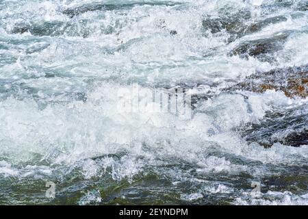 Schnelle Quelle Fluss über Felsen an sonnigen Tag, bilden weiße Wasserwellen, Nahaufnahme Detail - abstrakte Natur Hintergrund Stockfoto