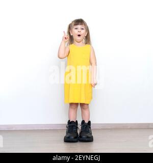 Kleines Mädchen in großen Papa Stiefel stehen über grauen Hintergrund mit Überraschung Gesicht zeigt Finger nach oben, Idee Konzept Stockfoto