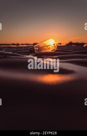 Glühbirne im Sand, die von der Sonne beleuchtet wird Bei Sonnenuntergang Stockfoto