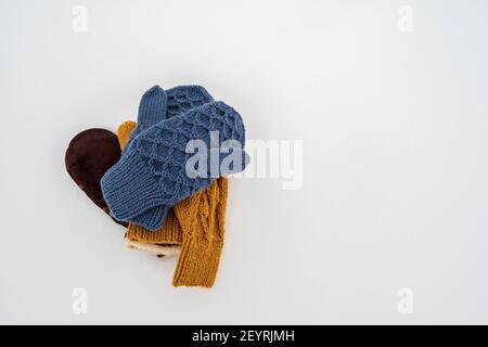 Mehrere Paare gestrickter, warmer Fäustlinge liegen auf weißem, sauberem Schnee, an einem bewölkten Wintertag im Stapel. Speicherplatz kopieren. Stockfoto