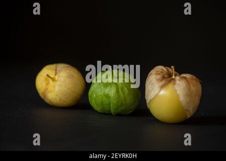 Drei Tomatillos aufgereiht auf schwarzem Hintergrund, aus der Perspektive des Abendessens betrachtet - California Produce Konzept Stockfoto